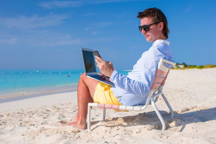 Young businessman using laptop and telephone on tropical beach