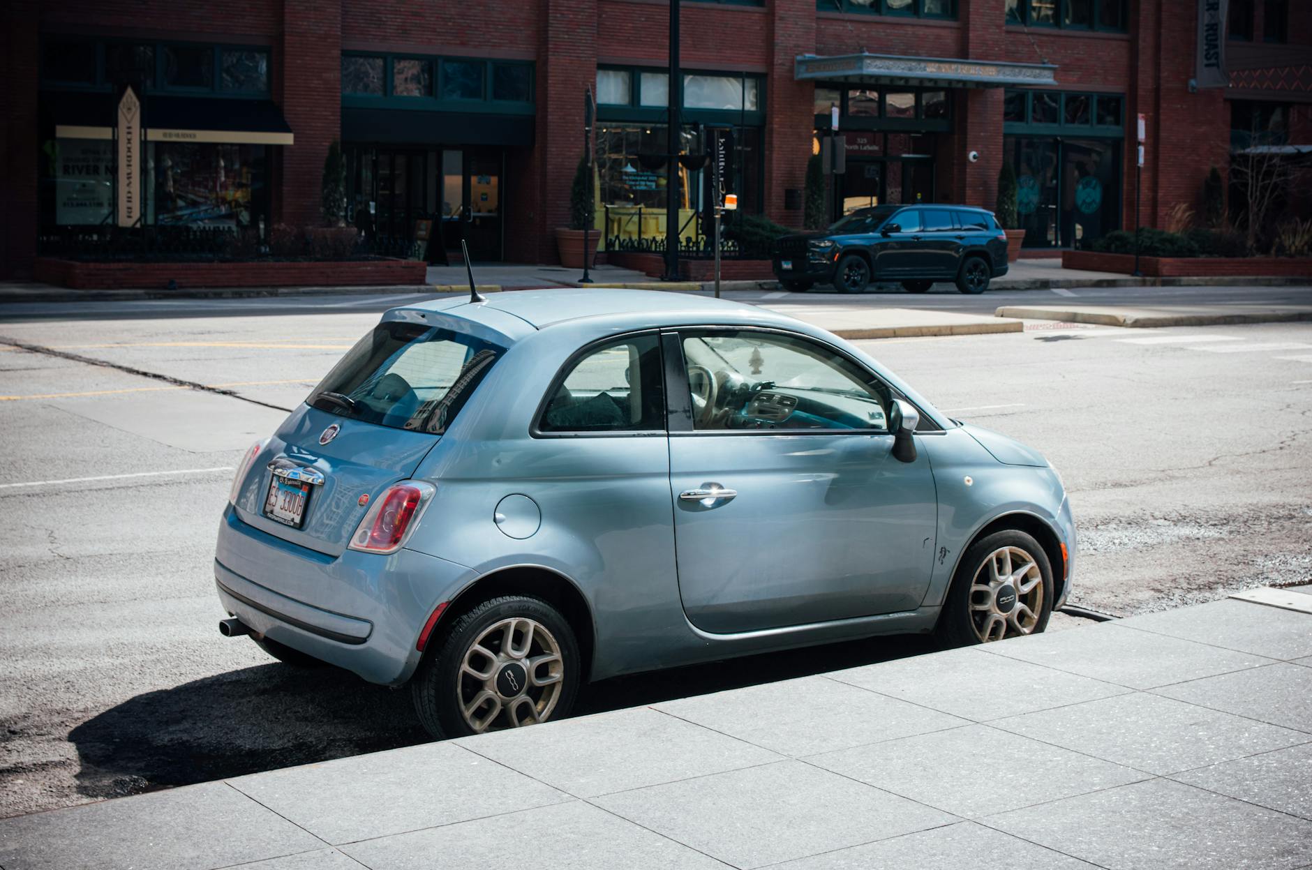 Niebieski Fiat 500 zaparkowany przy ceglanej kamienicy w dużym mieście